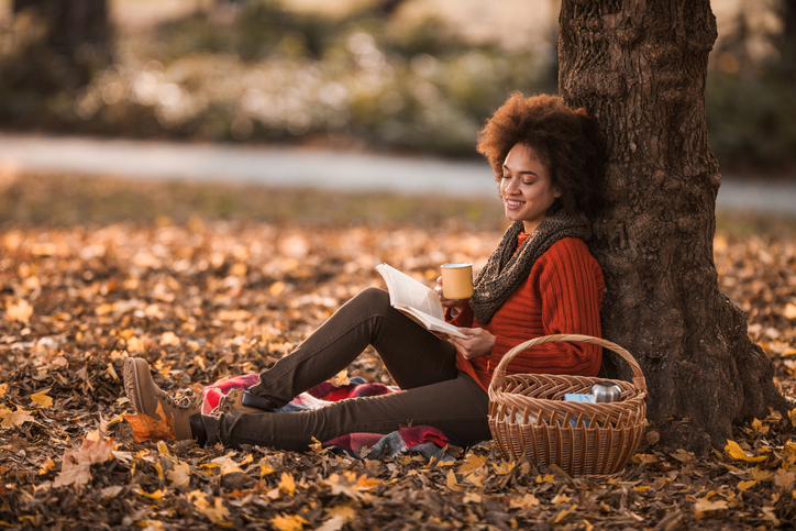 Happy black woman reading a book while enjoying on picnic in autumn day.