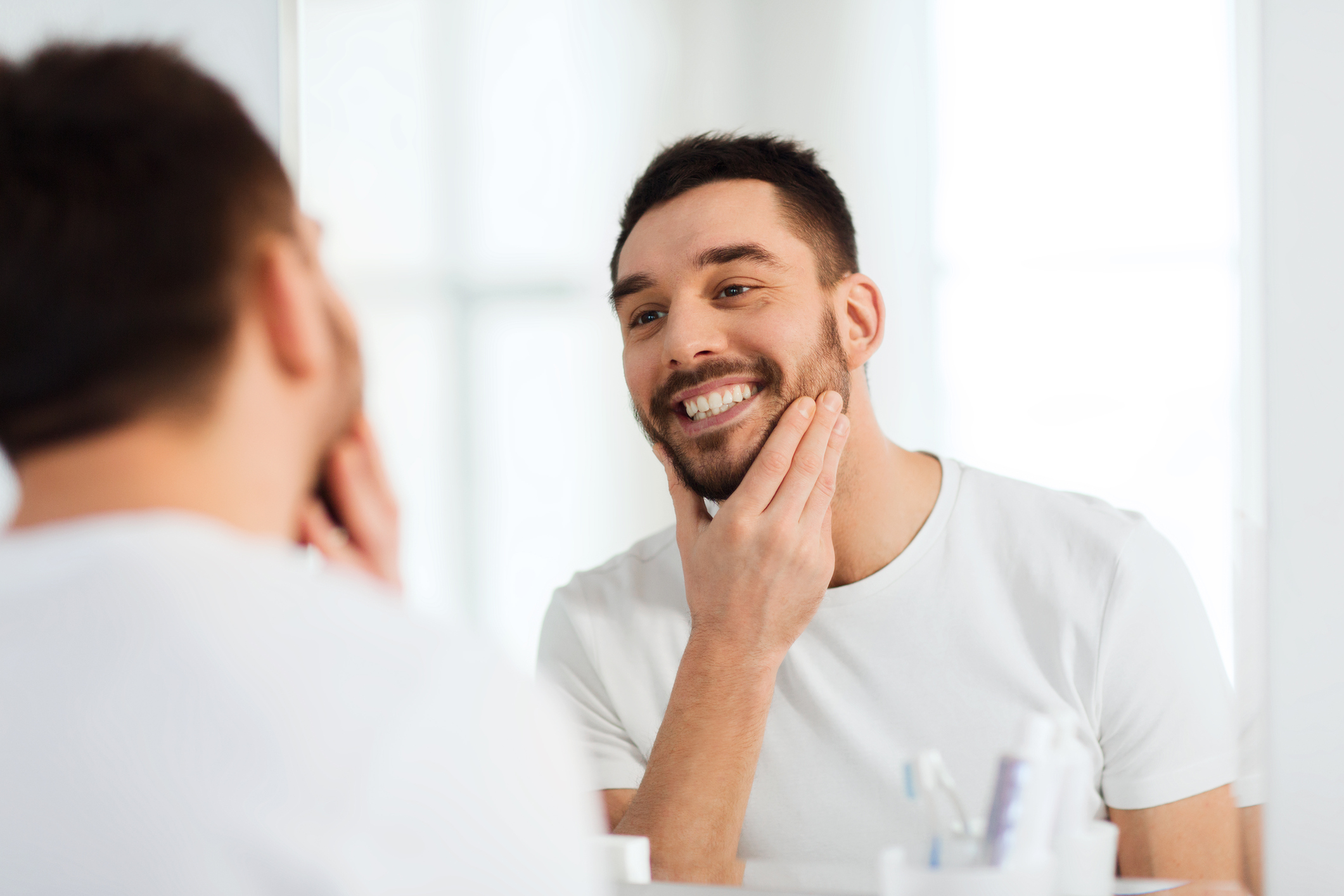 happy young man looking to mirror at home bathroom